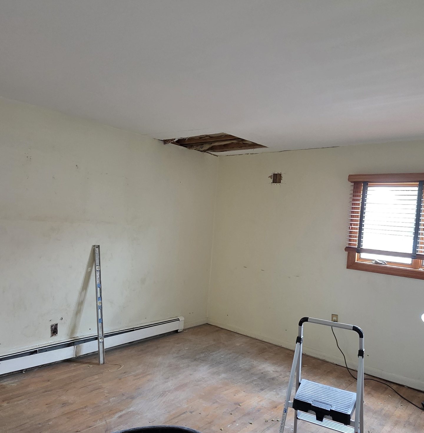 Primary bedroom before the work began, with an open ceiling hole from a leak and worn flooring