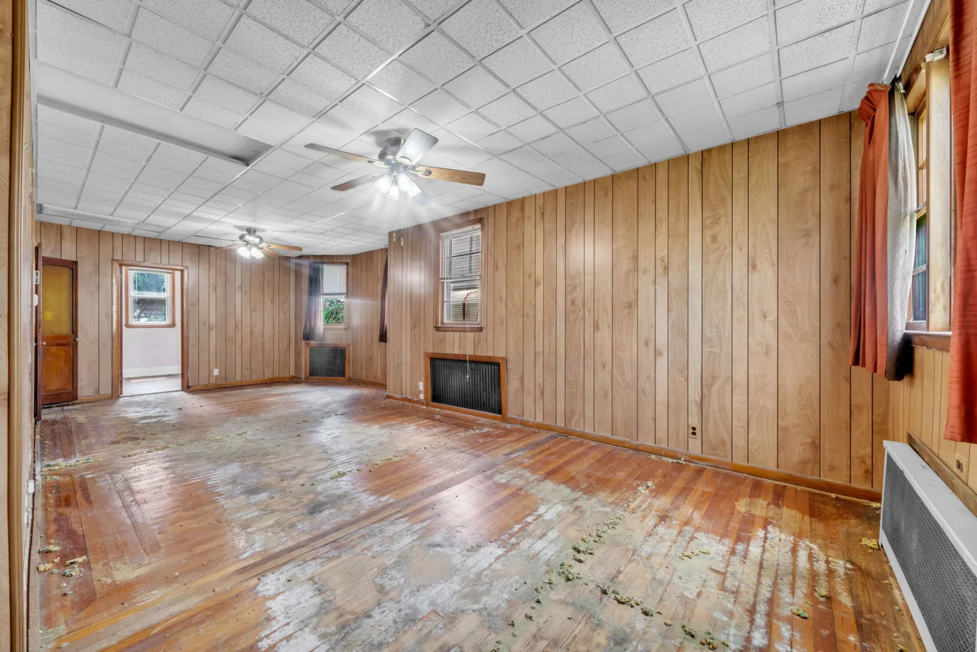 Vacant room with paneled walls and unfinished hardwood flooring during property preparation.