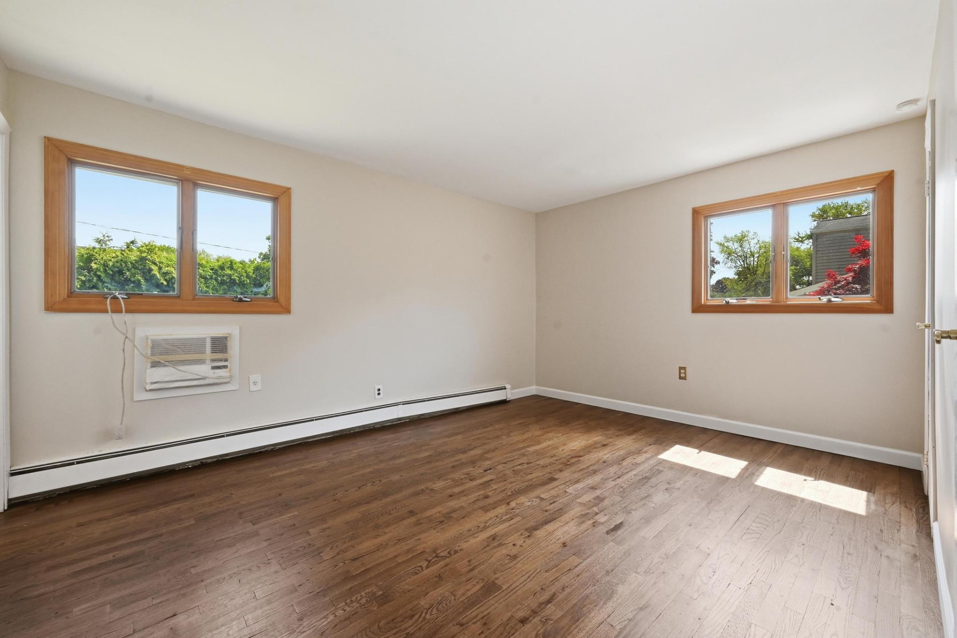 The same primary bedroom after the work, with refinished hardwood floors and repaired walls and ceiling