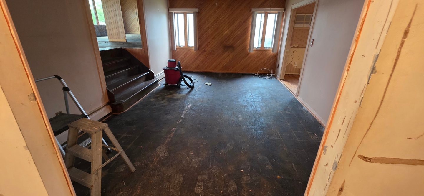 An emptied interior room with bare subfloor and stripped walls