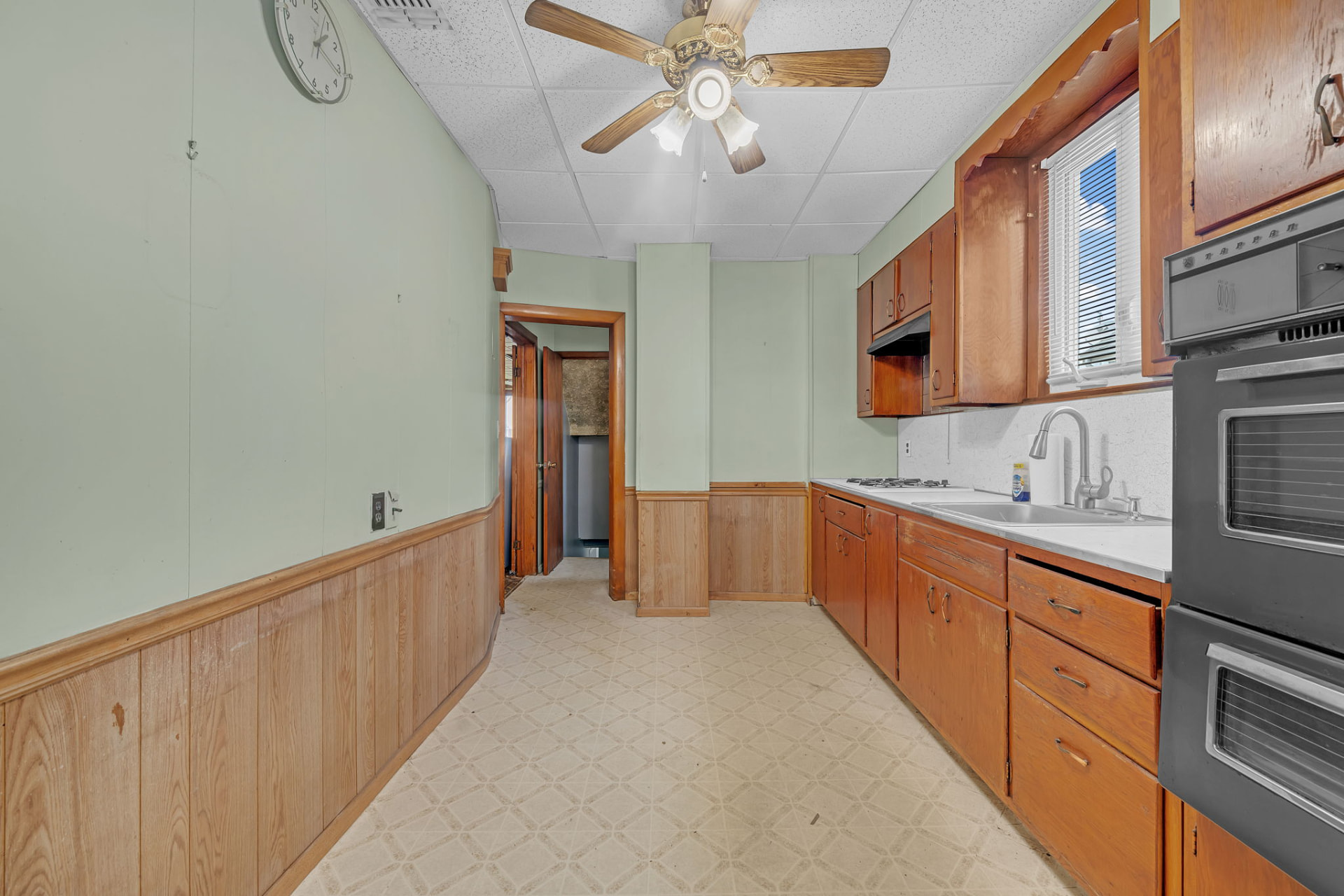 Kitchen with original wood cabinets, paneled walls and dated appliances during the preparation work.