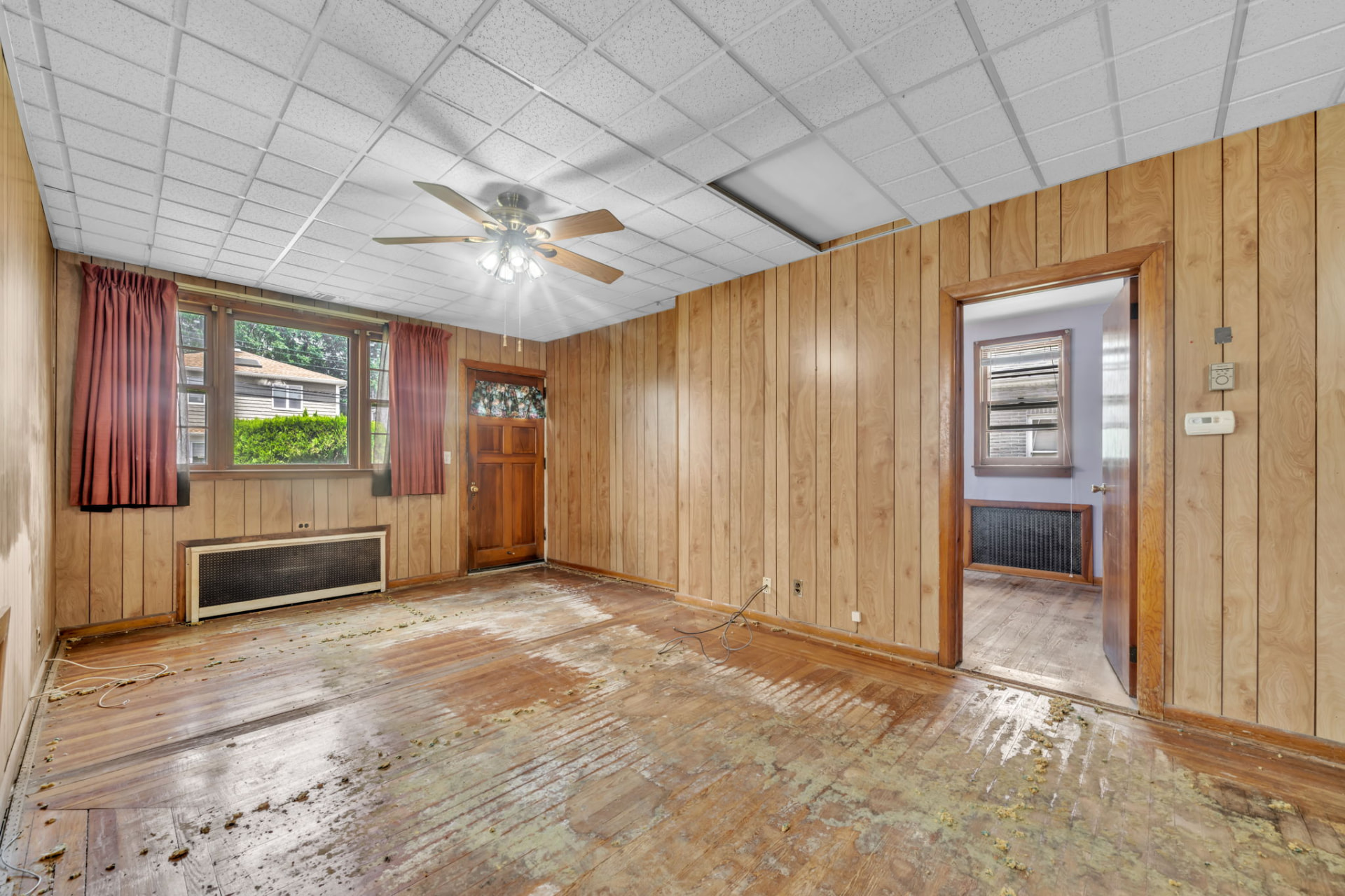 Vacant living room with paneled walls, unfinished flooring and a damaged ceiling during the preparation work.